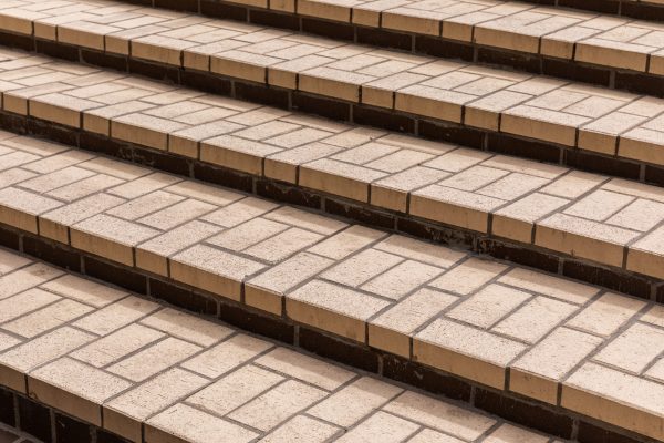Beige tiles of different shapes on the steps of concrete staircase, diagonal view.
