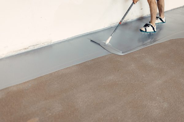 Construction worker applying epoxy resin on concrete floor using a trowel