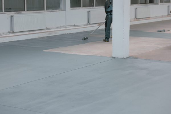 Worker paints the concrete floor with liquid gray paint